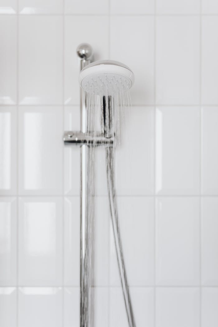 gallery-4 Chrome showerhead with flowing water on white tiled wall, depicting modern bathroom aesthetics.