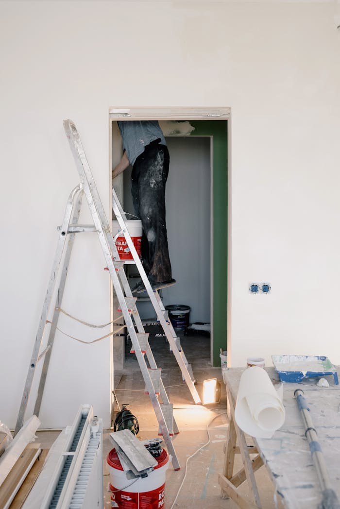 gallery-5 Indoor scene of home renovation with ladders, tools, and paint buckets.