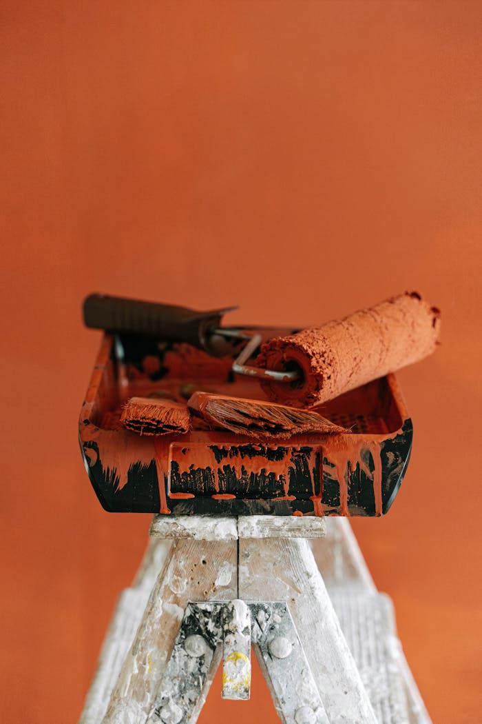 A stepladder holds paint tools for a vibrant orange home renovation project.